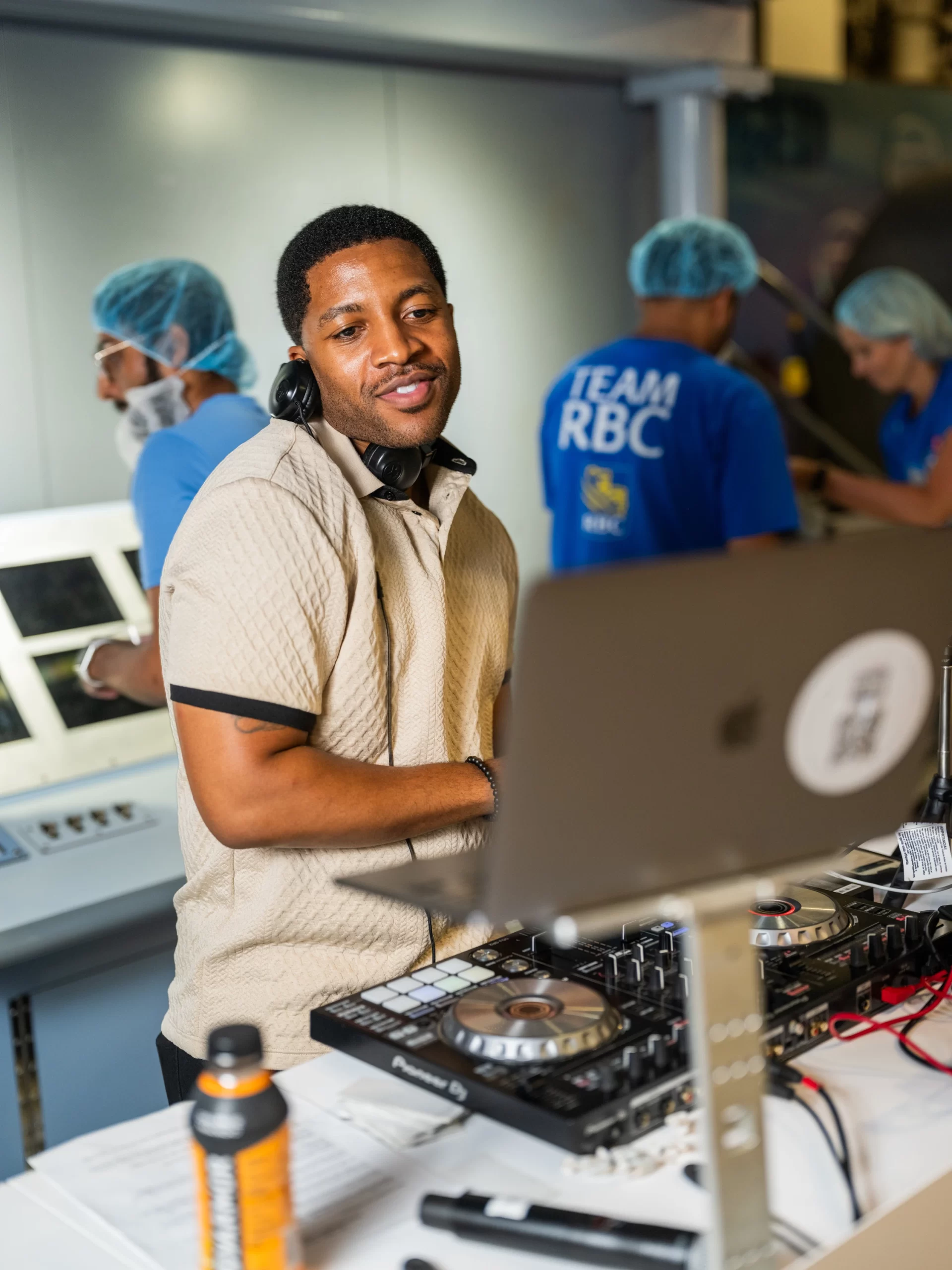 DJ Reese at the DJ booth while volunteers in hairnets pack meal kits behind him at the 9/11 Day Meal Pack in New York City