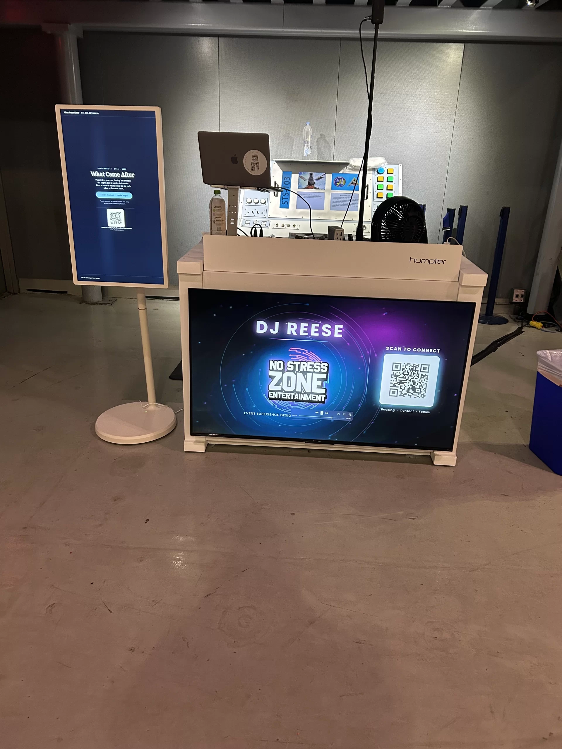 Touchscreen audience engagement kiosk running the 25th anniversary 9 11 Day trivia app, standing beside the branded No Stress Zone Entertainment DJ TV booth at the Intrepid in New York, September 2026